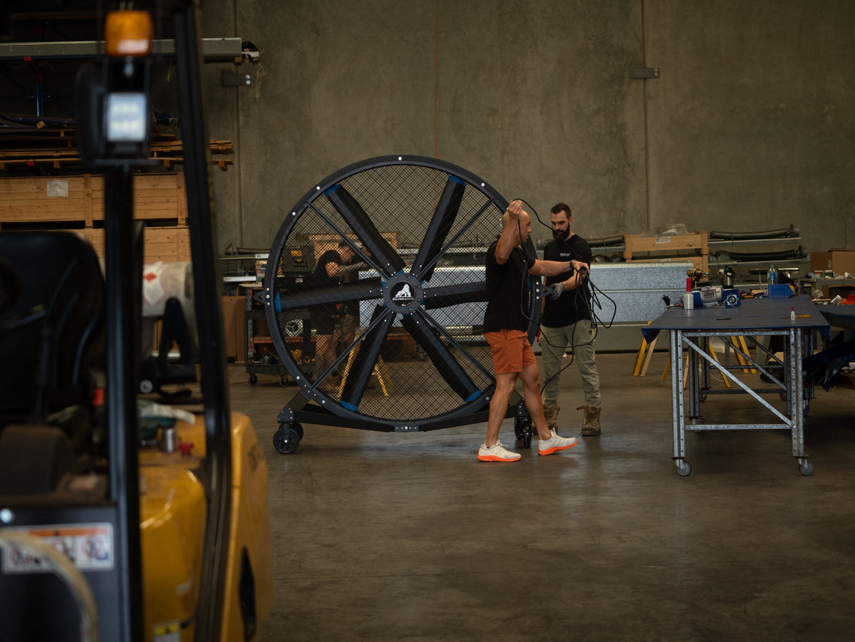 Two people rolling a Switchblade fan across a warehouse floor